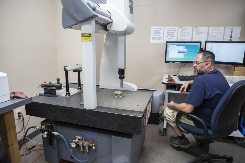 Apex Team Member Sits as CMM machine measures and quality checks a part.